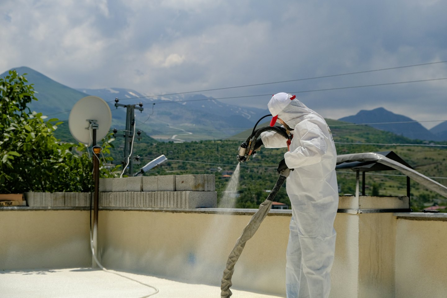Operaio in tuta protettiva spruzza isolamento sul tetto con cielo coperto.